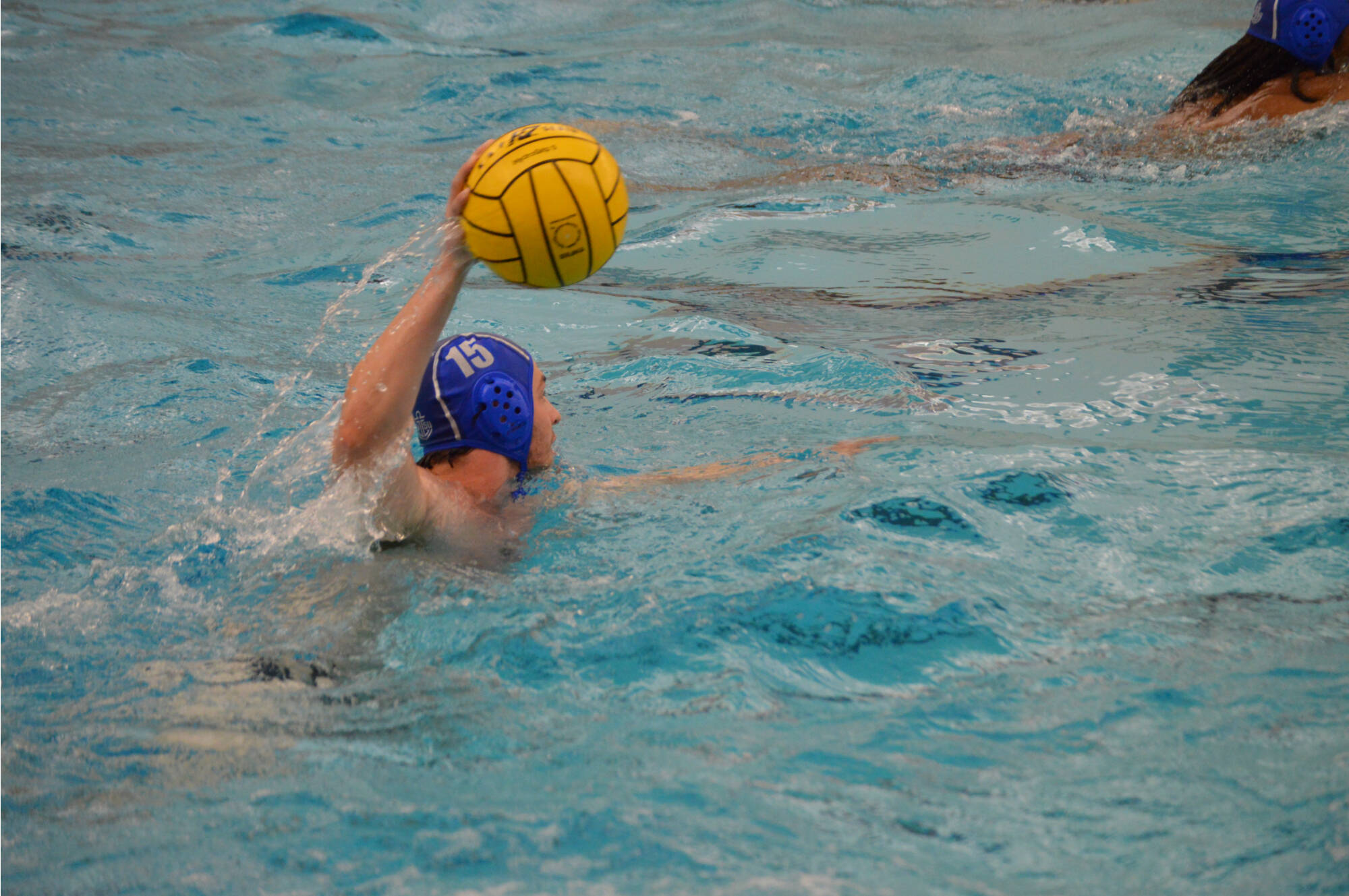 Water polo player (15) holding ball over his head.